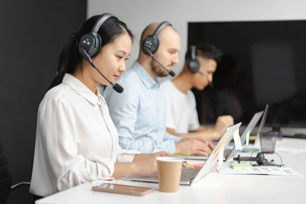 A woman and 2 men working with a headset in front of a laptop on a long table.